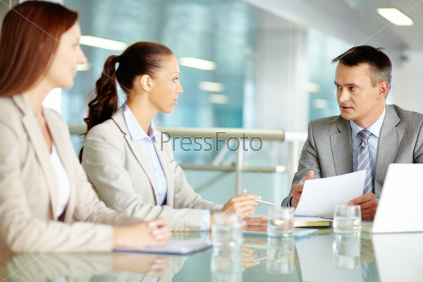 Serious boss looking at his employees while commenting a document at meeting