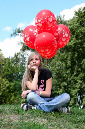 The girl - teenager sits on a grass with red balloons, stock photo
