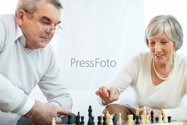 Portrait of senior woman pointing at chess-man while playing chess at leisure with her husband near by