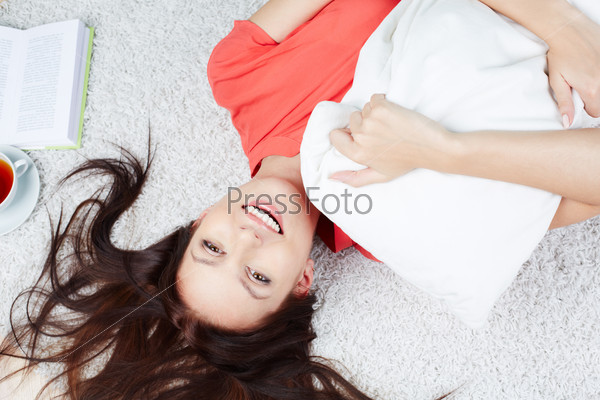Portrait of a cheerful woman with pillow lying on the floor
