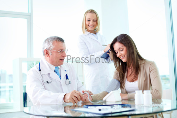 Portrait of male practitioner measuring blood pressure of patient with nurse near by, stock photo