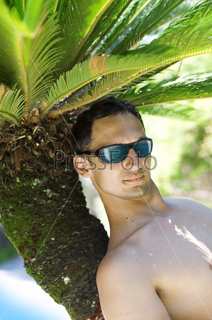 Fashion man lying upon palm tree on the beach