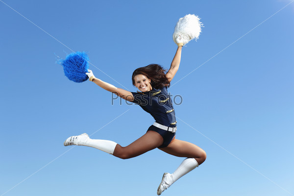 Young cheerleader in green costume jumping against blue sky, stock photo