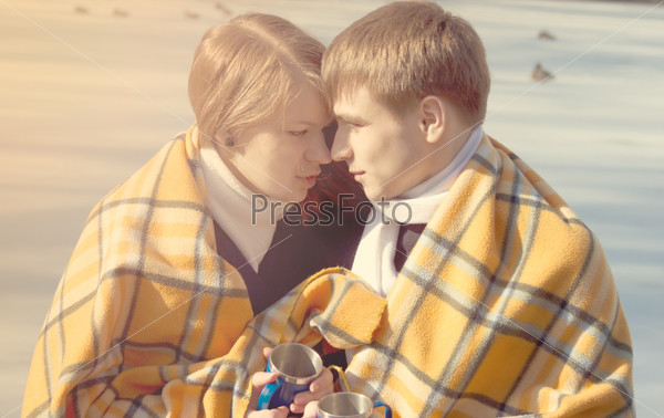 A young couple in love hugging wrapped in winter yellow plaid and drink tea