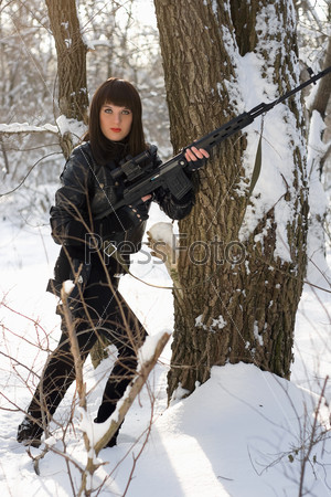 Young woman with a sniper rifle near the tree