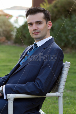 Handsome young man sitting outdoors in expensive suit
