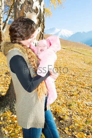 Happy young mother playing with little daughter in autumn park