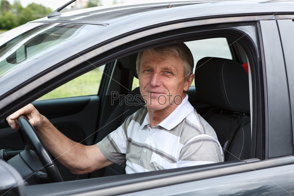 Happy senior male sitting in car on driver seat and smiling