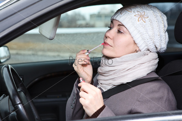 Beautiful woman in winter clothes in car applying make up