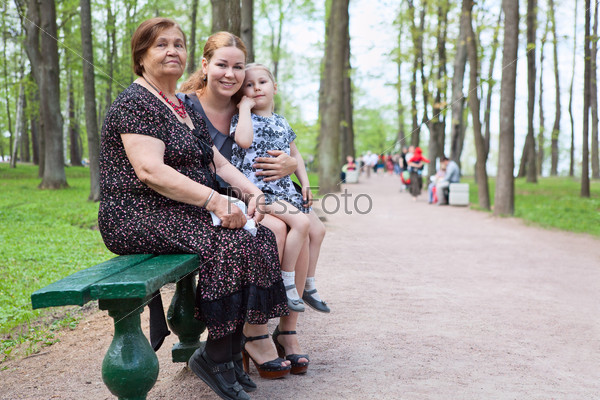 Three women different ages are sitting on bench in park. Grandmother, mother and small daughter