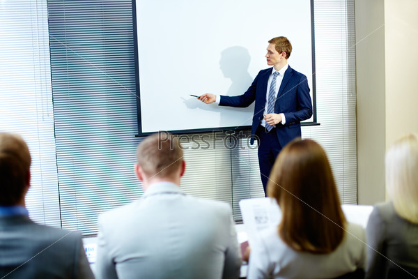 Confident businessman pointing at whiteboard while making speech at conference