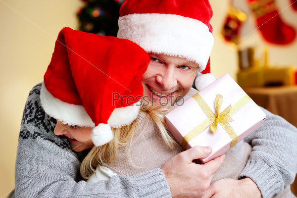 Portrait of happy man with giftbox embracing his joyful wife on xmas day