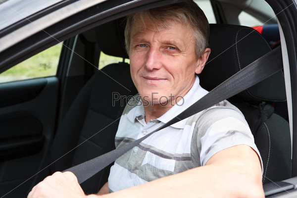 Happy Caucasian senior male fastens safety belt sitting in car on driver seat