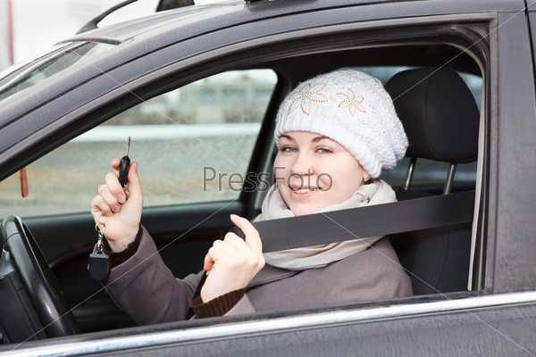 Happy woman sitting in car and holding ignition keys in hand
