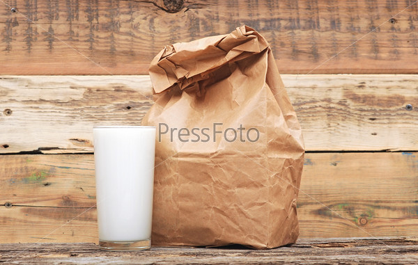 Бумажный мешок с обедом с стакан молока на деревянном фоне