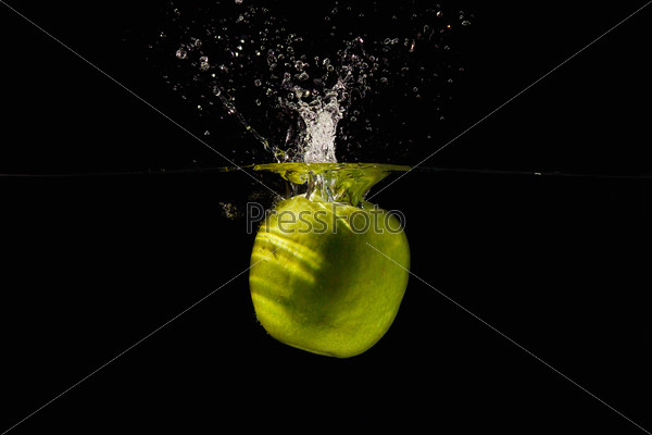 Ripe green apple falling into the water with a splash on a black background closeup