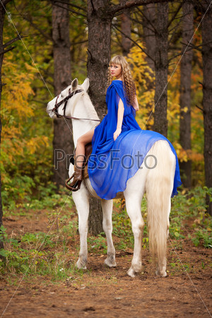 Young girl riding a white horse in the autumn park