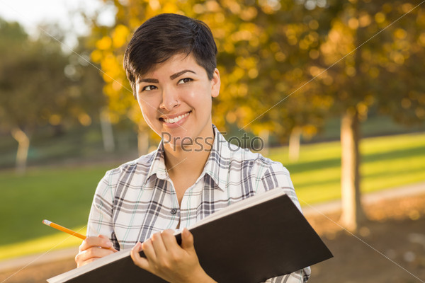Portrait of a Pretty Mixed Race Female Holding Sketch Book and Pencil Outdoors at the Park on a Sunny Afternoon.