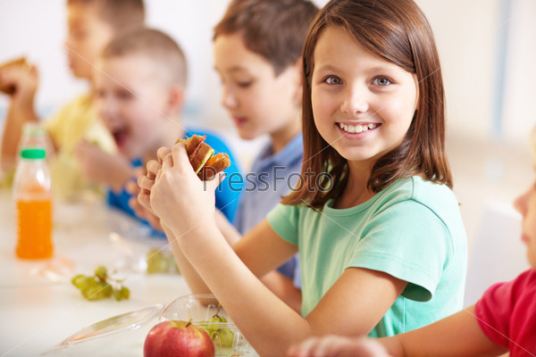 Group Of Classmates Having Lunch During Break With Focus On Smiling Girl With Sandwich