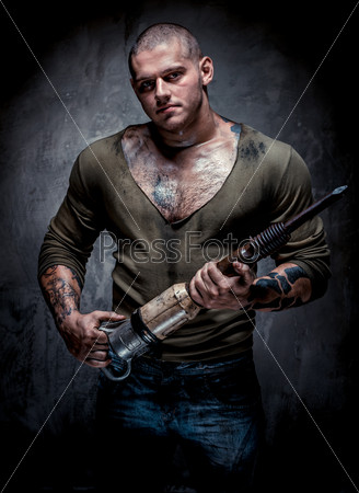Muscular tattooed man with jackhammer posing over grey background