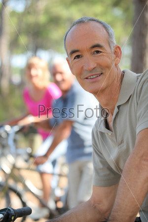 Older man riding a bike in the forest with friends