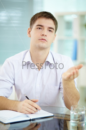 Portrait of young businessman explaining something while making notes in notepad