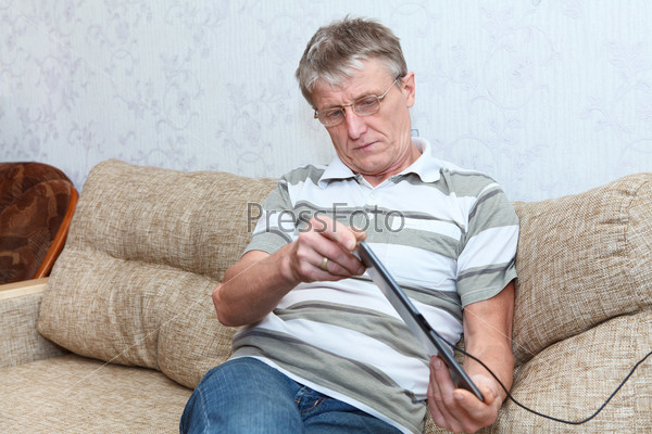 Mature adult Caucasian man researching at a new tablet pc in domestic room