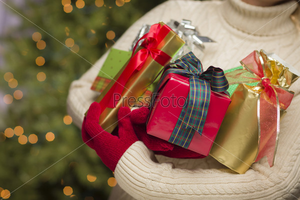 Woman Wearing A Sweater and Seasonal Red Mittens Against an Abstract Green and Golden Background Holding Beautifully Wrapped Christmas Gifts.