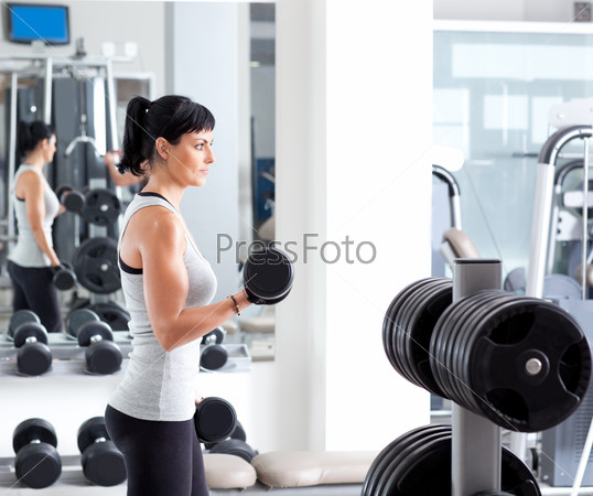 Gym fitness club indoor with young woman training weights on mirror