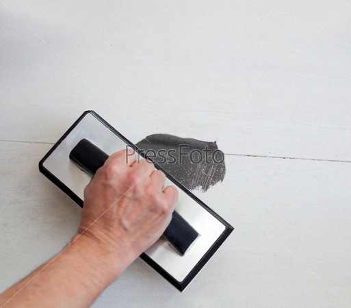 grouting tiles with rubber trowel and gray cement mortar