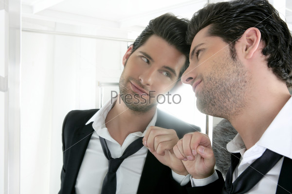Красивый молодой человек в костюме самовлюбленно смотрит в зеркало