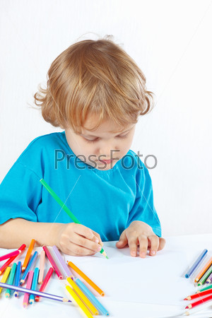 Little cute blond boy draws with color pencils on a white background