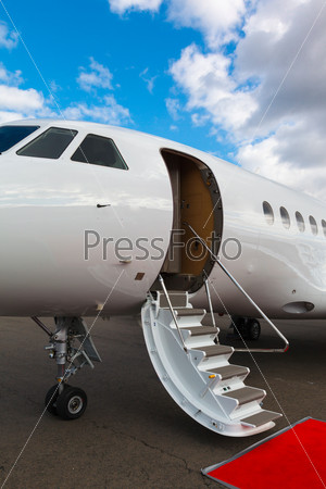 white private jet and open ladder, red carpet at the airport on a background blue sky