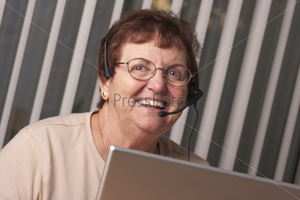 Smiling Senior Adult Woman with Telephone Headset In Front of Computer Monitor.