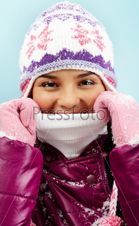 Face of pretty woman in knitted winter cap and gloves looking at camera