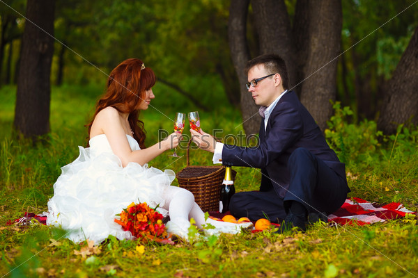 in Russia newlyweds couple bride and groom sitting on green grass, a picnic in woods at wedding drink wine