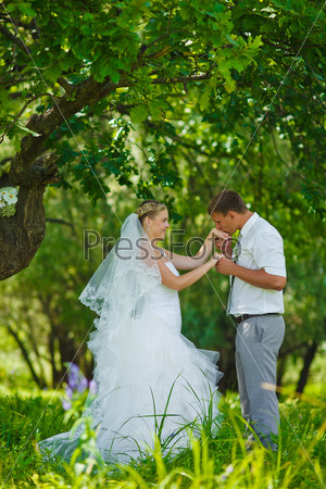 bride groom kissing hand of blonde bride, newlyweds couple are in a green forest in wedding summer