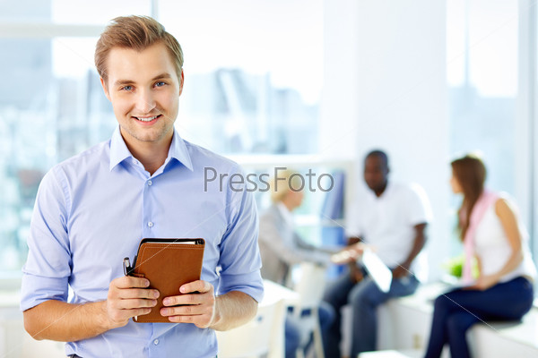 Portrait of happy man with notepad looking at camera in working environment