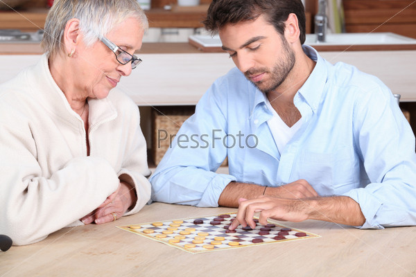 Молодой человек играет в шашки с пожилой женщиной