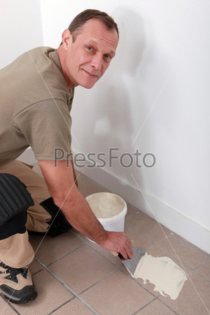 Decorator spreading adhesive on a tiled floor