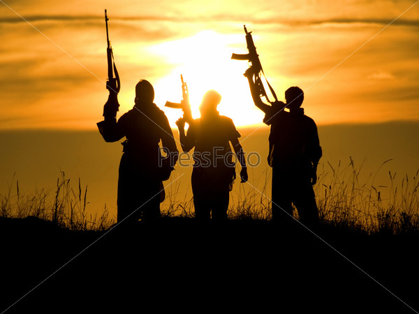 Silhouettes of several soldiers with rifles against a sunset