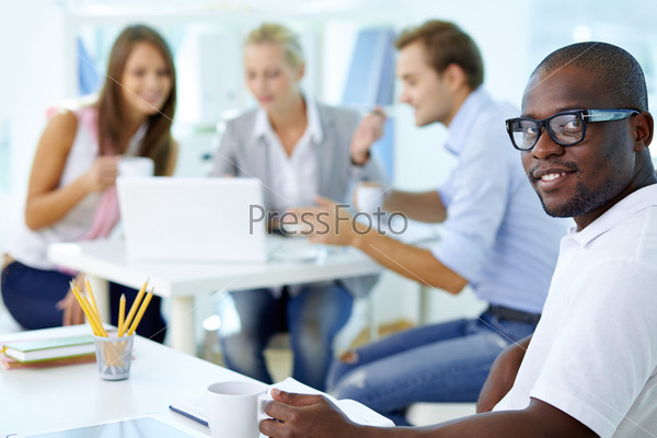 Portrait of happy African guy looking at camera in working environment