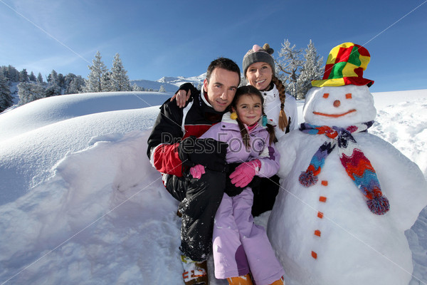 couple posing with child beside snowman at mountain resort