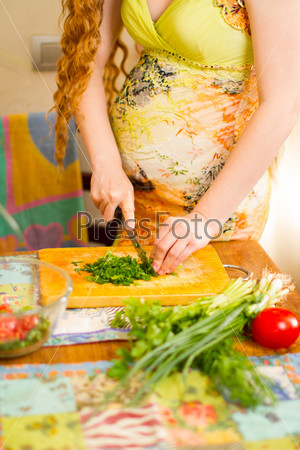 Pregnant woman s hands and belly cutting on kitchen with healthy food The concept of food and a healthy lifestyle