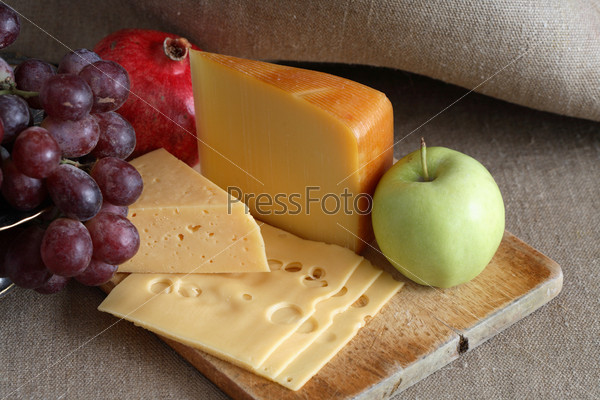 Still life with few sorts of cheese and fruits on wooden hardboard
