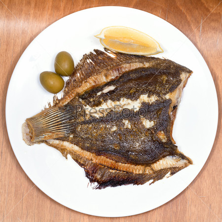top view of fried sole fish on white plate on wooden table