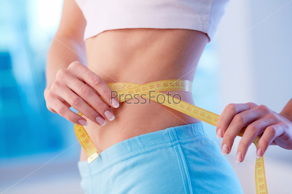 Close-up of a fit female with slim waist and a measuring tape