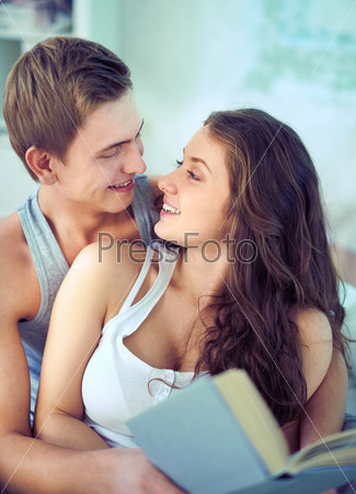 Portrait of amorous young man talking to his girlfriend while she reading book