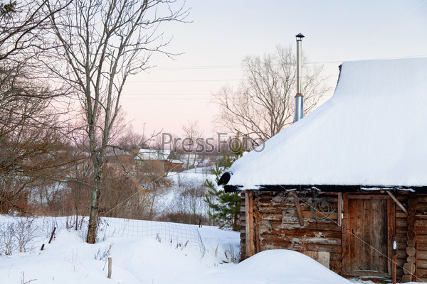 snow-covered wooden house in country at pink winter sunset