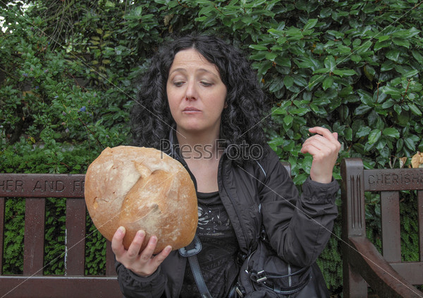 To eat or not to eat - Portrait of pretty young brunette looking at huge bread in hamletic pose